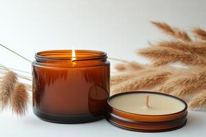Aromatic candle lit beside decorative dried grass on white surface during tranquil setting photo