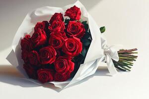 A beautiful bouquet of vibrant red roses wrapped delicately in white paper with bow photo