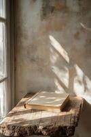 A blank book resting on a rustic wooden table near a light filled window in a cozy room photo