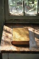 A leather bound book resting on a rustic wooden table near a sunny window with plants photo