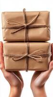 Hands holding stacked wrapped packages tied with twine against a plain background photo