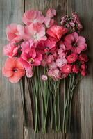 A vibrant collection of various pink flowers arranged artistically on a rustic wooden surface photo