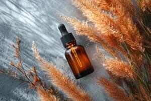 Brown glass dropper bottle on textured surface with decorative dried plants in autumn setting photo