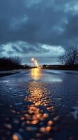 Wet road reflecting streetlights under a moody sky during dusk photo