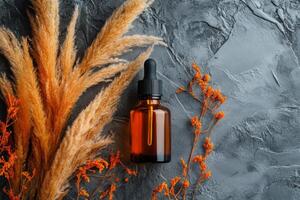Brown glass dropper bottle on textured surface with decorative dried plants in autumn setting photo