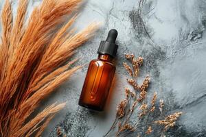 Brown glass dropper bottle on textured surface with decorative dried plants in autumn setting photo