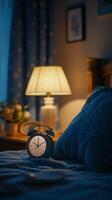 Cozy bedroom with a bedside clock and lamp featuring floral wallpaper at night photo