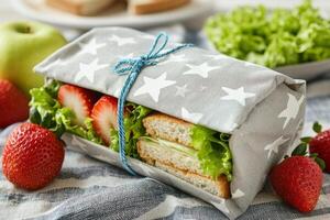 Freshly wrapped sandwich with strawberries and lettuce on a textured cloth in a bright kitchen photo
