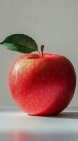 A fresh red apple with a green leaf resting on a white surface in natural light photo