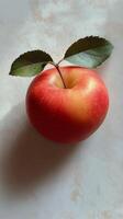 A fresh red apple with a green leaf resting on a white surface in natural light photo