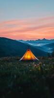 A vibrant tent lights up the dusk in a serene mountainous landscape at twilight photo