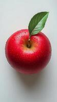 A fresh red apple with a green leaf resting on a white surface in natural light photo