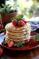 Delicious stack of fluffy pancakes topped with fresh strawberries and maple syrup on a cozy table photo