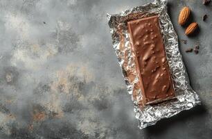 Rich chocolate bar wrapped in foil on a textured gray surface photo