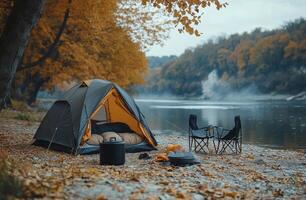 Cozy tent set up by a tranquil riverbank surrounded by autumn foliage in the wilderness photo