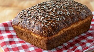 Freshly baked whole grain bread topped with sunflower seeds on a checkered cloth photo