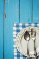 Rustic dining setup with vintage cutlery on blue wooden table with checkered napkin photo