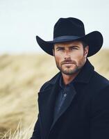 Man in black hat poses confidently in a golden field on a cloudy day photo