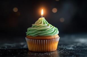 Delicious green frosted cupcake with a lit candle against a dark background photo