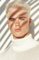 Young man with light hair poses in shadows and light from window blinds photo