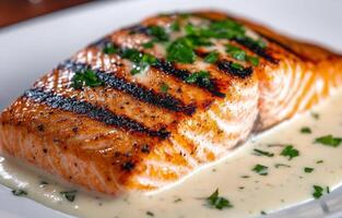 Grilled salmon filet served with creamy sauce and fresh herbs on a white plate photo