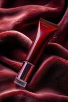 Glossy red cosmetic tube resting on soft burgundy fabric in a cozy setting photo