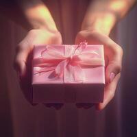 Delicate hands presenting a small pink gift box tied with a ribbon in soft lighting photo