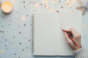 Person writing in a blank notebook with candle and decorative stars during holiday season photo