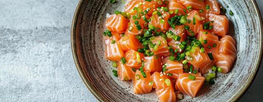 Fresh salmon sashimi served in a decorative bowl with scallions and sesame on a dark table photo
