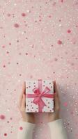 A person holds a gift with a red ribbon against a sparkling pink background photo