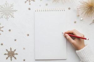 Person writing in a blank notebook with candle and decorative stars during holiday season photo