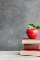 Red apple placed on top of stacked red books against a neutral gray background indoors photo