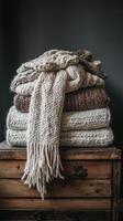 Cozy knitted blankets draped over a rustic wooden stool in a warm, inviting interior setting photo