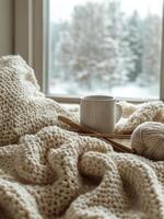 Cozy setup with knitted blanket, coffee cup, and yarn balls in a softly lit room during winter photo