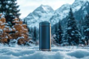 Metal reusable water bottle standing on snow in front of mountain range photo