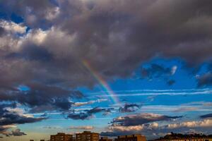 A colorful rainbow arcs across a dramatic sky filled with dark and light clouds photo