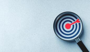 Target board icon in magnifying glass on white paper background. concept of finding goals and setting clear objectives. photo