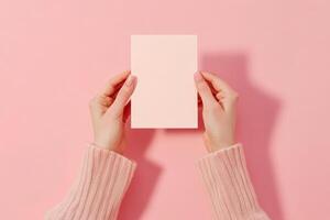 Hand holding printed greeting card mock up, blank empty postcard isolated pink on natural flower background photo