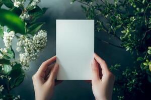 Hand holding printed greeting card mock up, blank empty postcard isolated on natural flower background photo