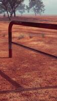 A rustic red dirt field with a charming fence and trees in the background video