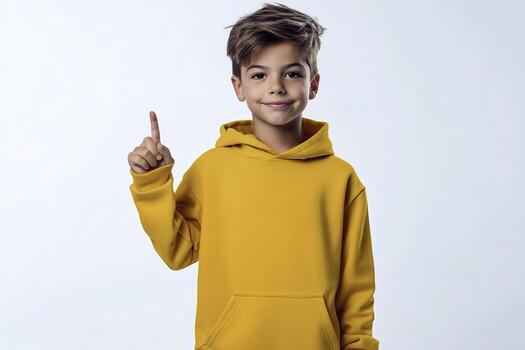 Little boy in yellow hoodie pointing finger up at copy space on the white background. photo
