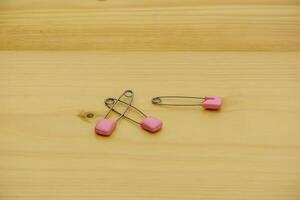 One open and one closed safety pin with pink caps lie on a wooden background. photo
