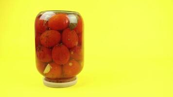 Overturned glass jar of closed tomatoes on a yellow background video