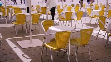 tables with yellow chairs and working waiters in street cafe video