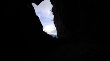 Entrance to dark cave on steep cliff against sky with clouds video