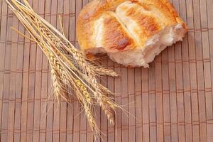 Piece of bread and spikelets of wheat on wooden background. Tasty bread on table close-up photo