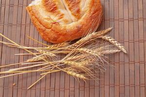 Piece of bread and spikelets of wheat on wooden background. Tasty bread on table close-up photo