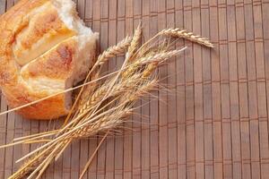 Piece of bread and spikelets of wheat on wooden background. Tasty bread on table close-up photo
