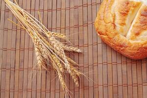 Piece of bread and spikelets of wheat on wooden background. Tasty bread on table close-up photo