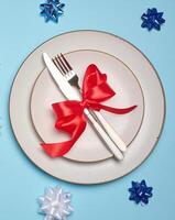 Round white plate and tied with red bow view with knife on a blue background, festive table setting photo